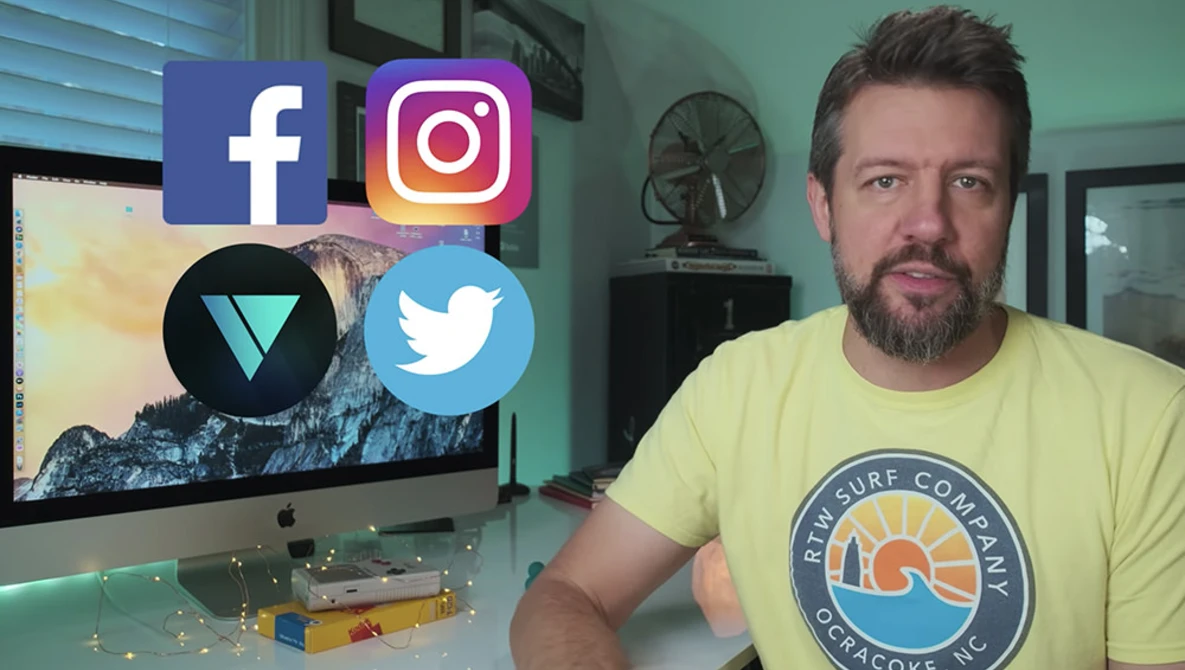 Man in yellow surf-themed t-shirt sitting at desk with monitor displaying social media platform logos.