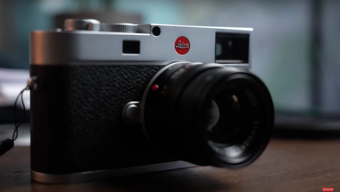 Leica M rangefinder camera with silver top plate and black body, shown with attached lens on wooden surface.