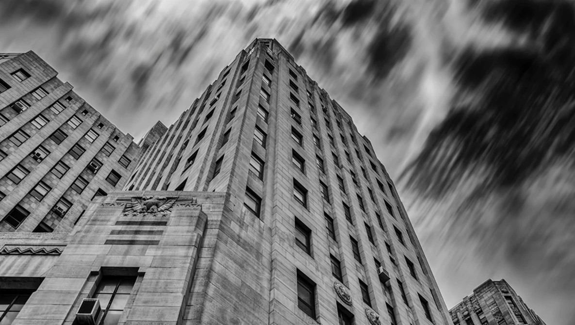 Upward view of tall Art Deco building with dramatic clouds and motion blur.