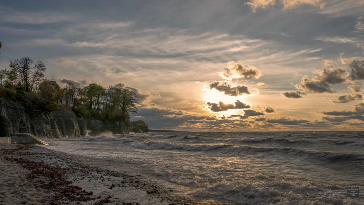 Dramatic coastal landscape with eroded cliff, beach, and golden sunset sky with storm clouds.
