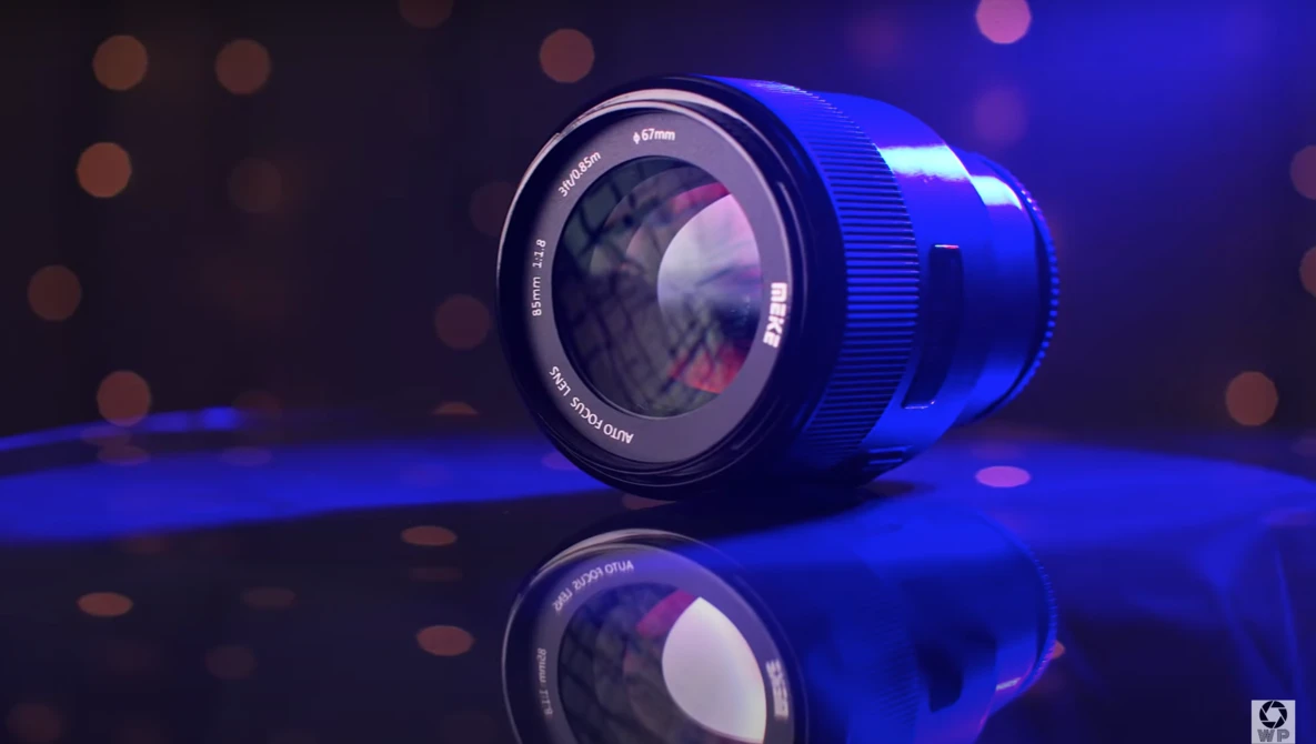 Prime camera lens with blue rim and text markings, positioned on reflective surface with blue accent lighting and bokeh background.