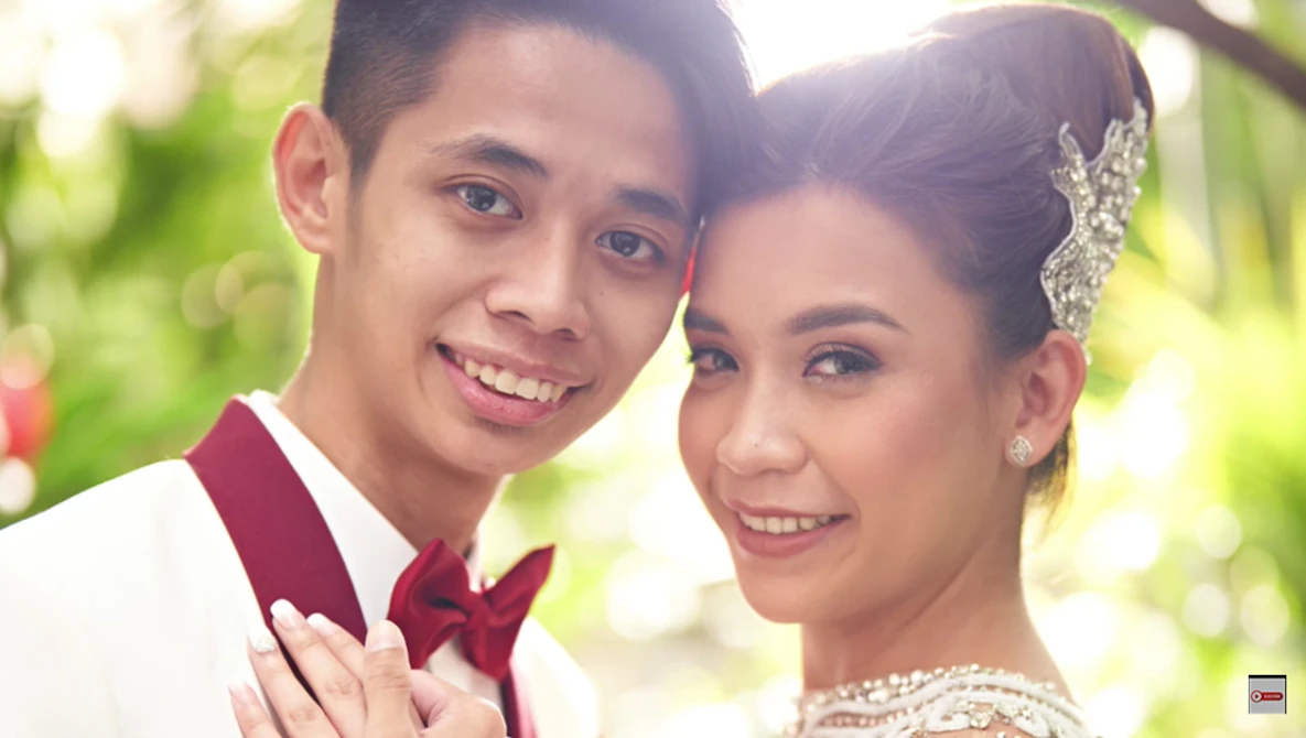 Young couple in formal wedding attire smiling outdoors in natural sunlight.