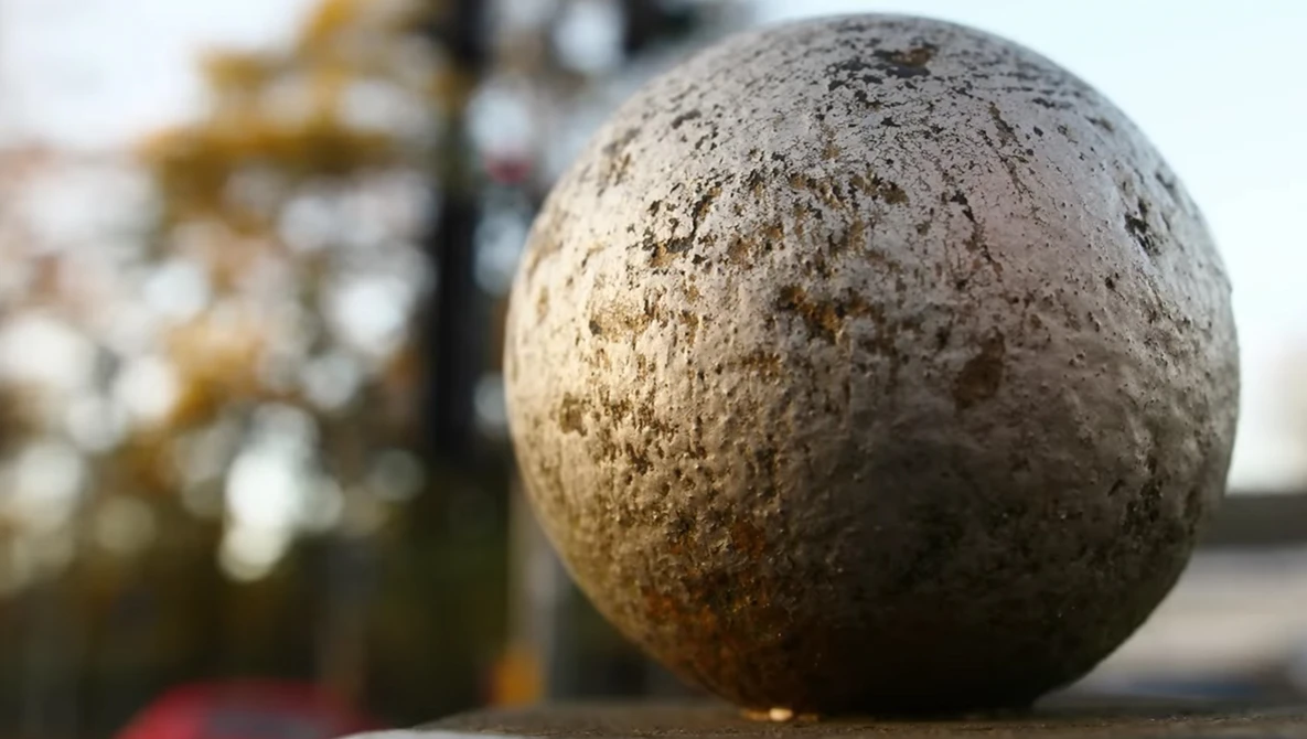 Close-up of a weathered concrete sphere with textured surface and golden-brown discoloration.