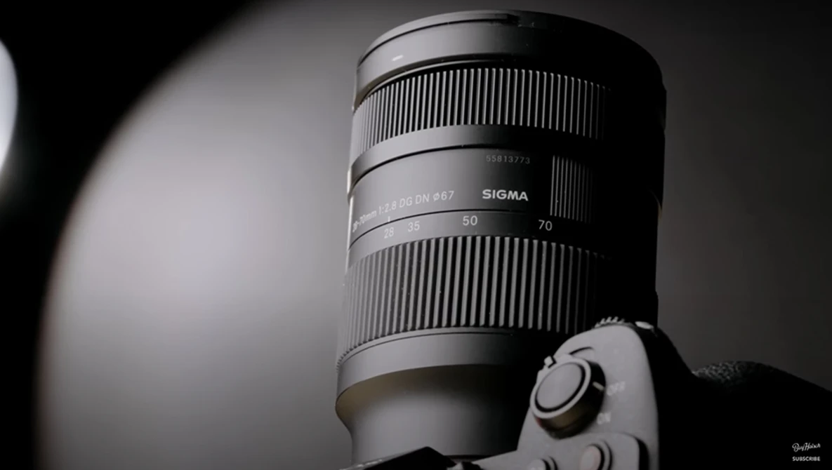 Sigma telephoto lens mounted on camera body, shown in black and white studio lighting.