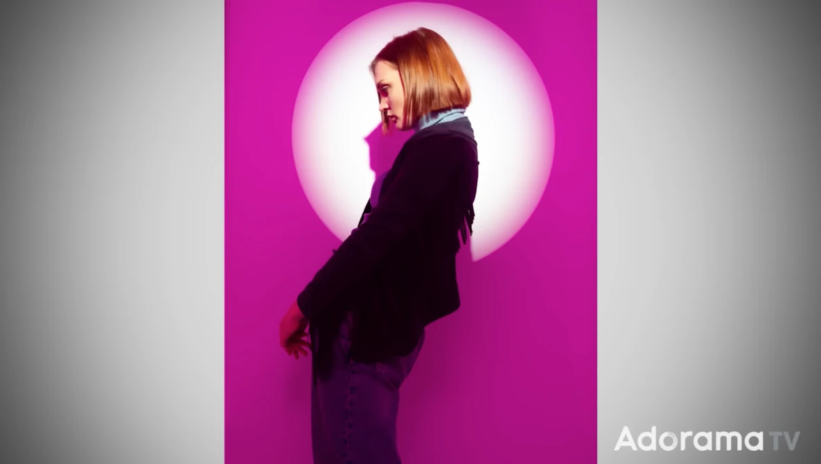 Woman in dark blazer photographed in profile against a bright circular magenta backdrop with soft halo lighting effect.
