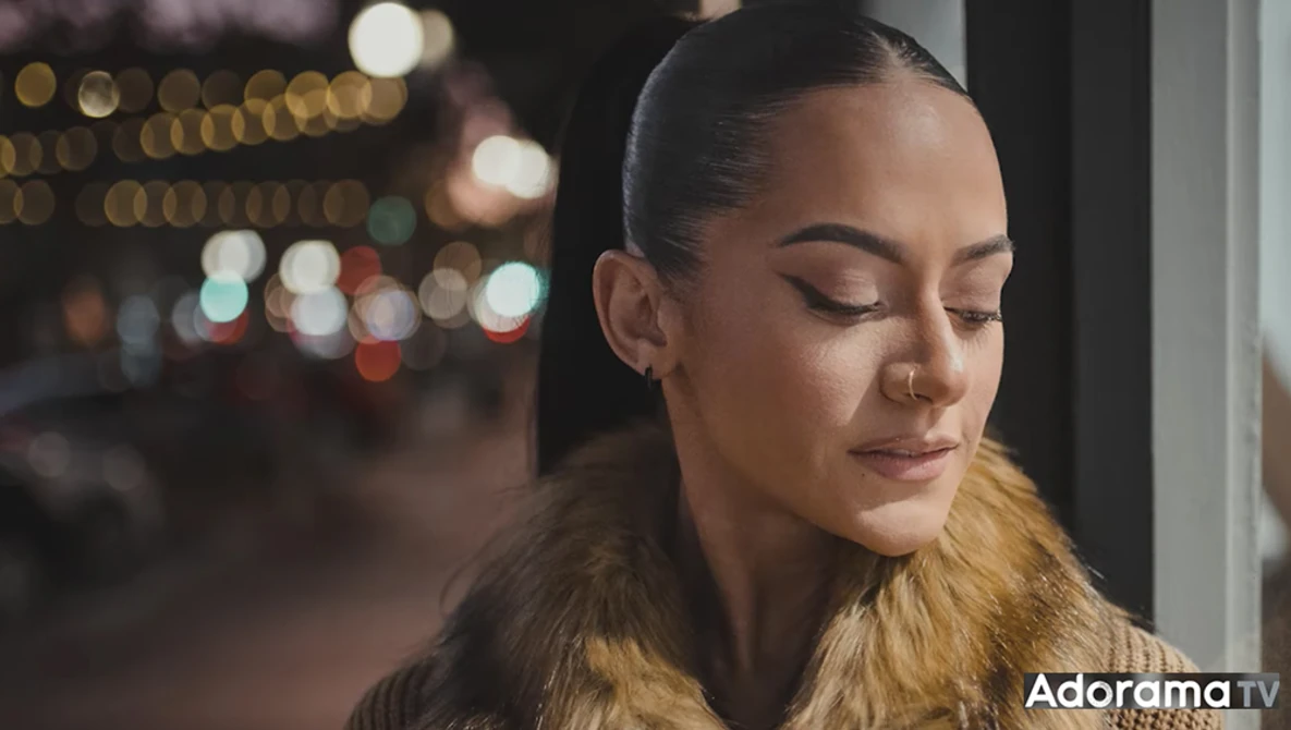 Woman with pulled-back hair looking downward against blurred city lights at night.
