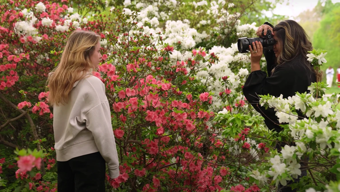 Photographer capturing portrait of woman posing among blooming pink and white flowers.
