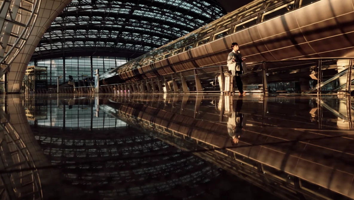 Modern train stationed in a glass-roofed terminal with mirror-like reflections on wet floor.
