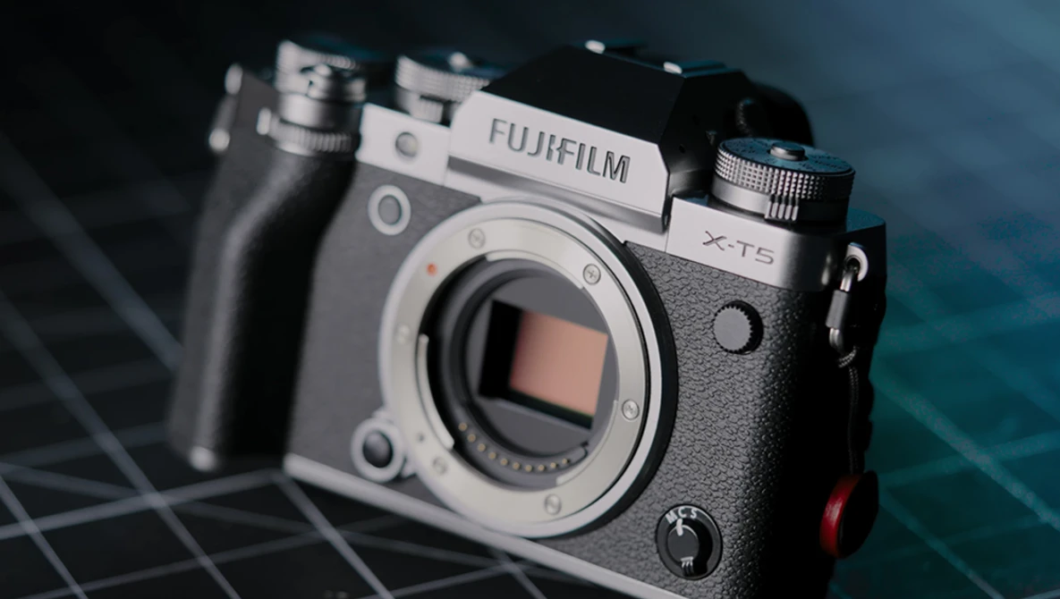 Fujifilm X-T5 mirrorless camera body displayed against a dark blue geometric background.