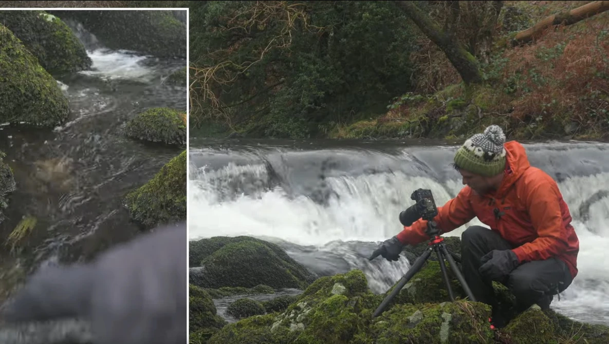 Photographer with tripod capturing a flowing waterfall in a moss-covered forest landscape.