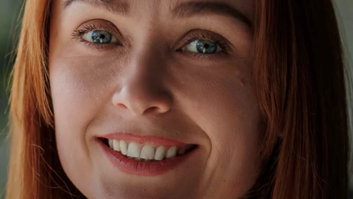 Close-up portrait of a woman with red hair and blue eyes smiling at camera.