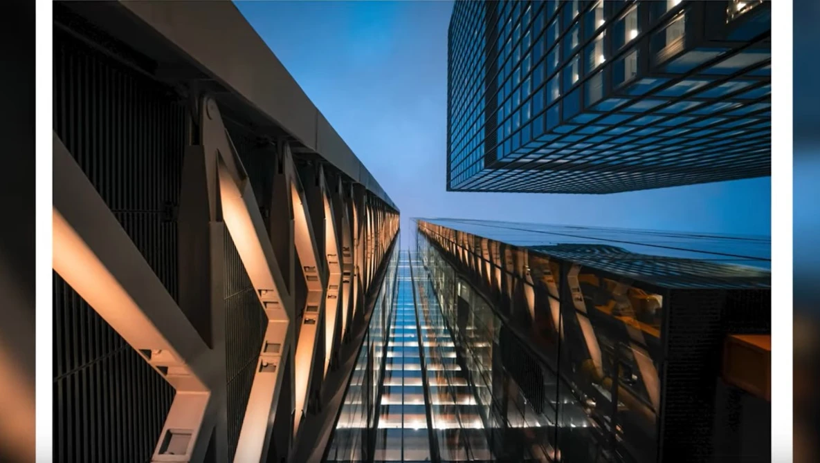 Upward perspective of modern skyscrapers converging toward clear blue sky with warm golden light across facades.