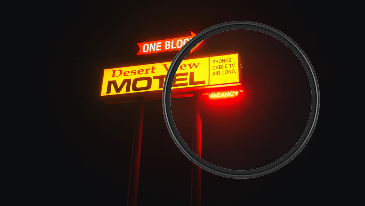 Vintage neon motel sign glowing red and yellow against dark night sky with magnifying glass overlay.
