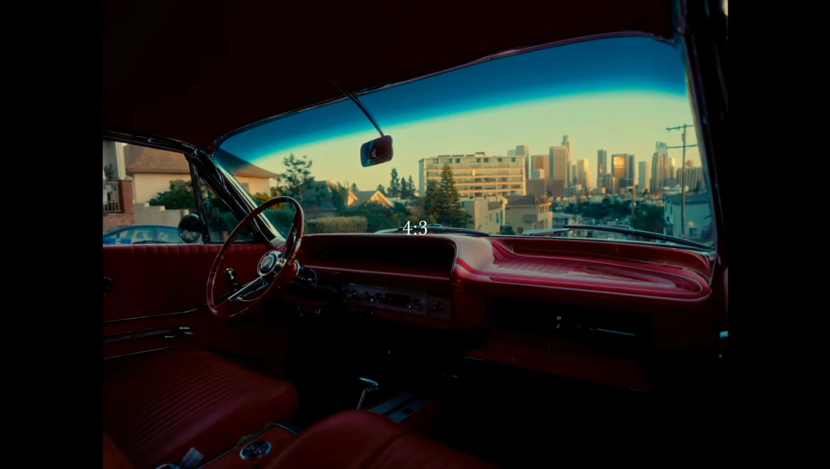View from inside a classic red car with city skyline visible through the windshield at golden hour.