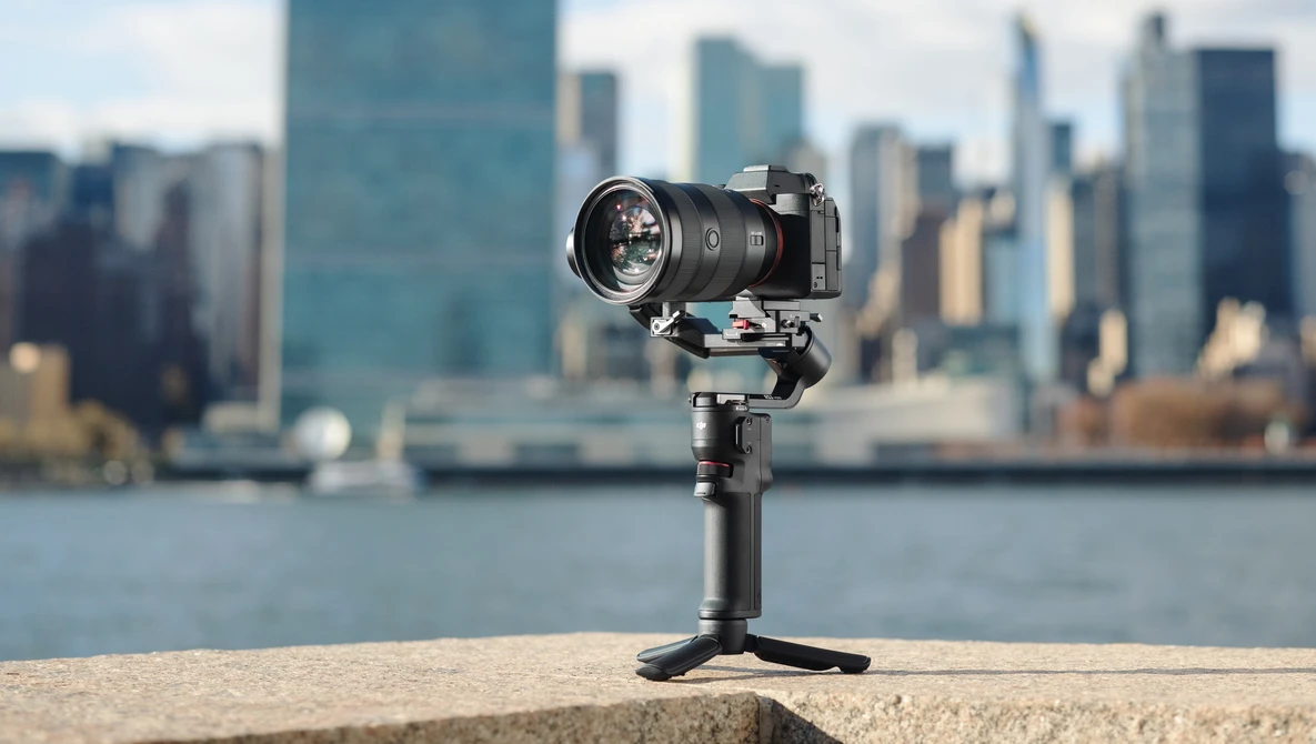 Compact camera gimbal mounted on concrete ledge with blurred cityscape and waterfront in background.