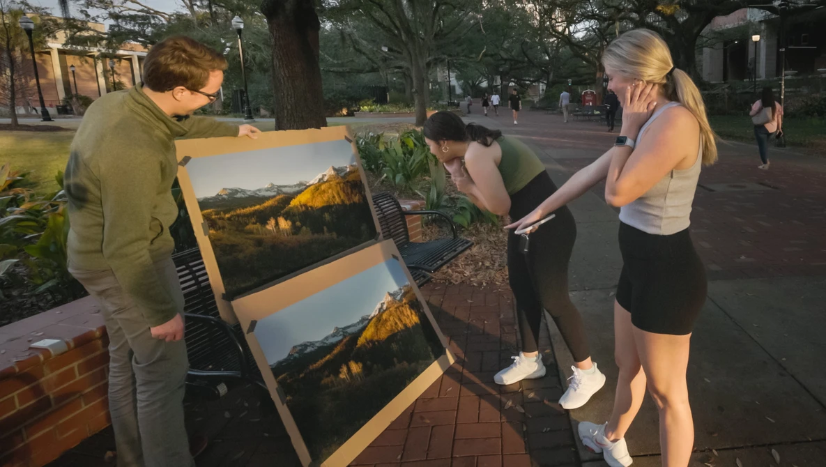 Street photographer displays landscape prints on an easel while passersby examine the work in natural evening light.