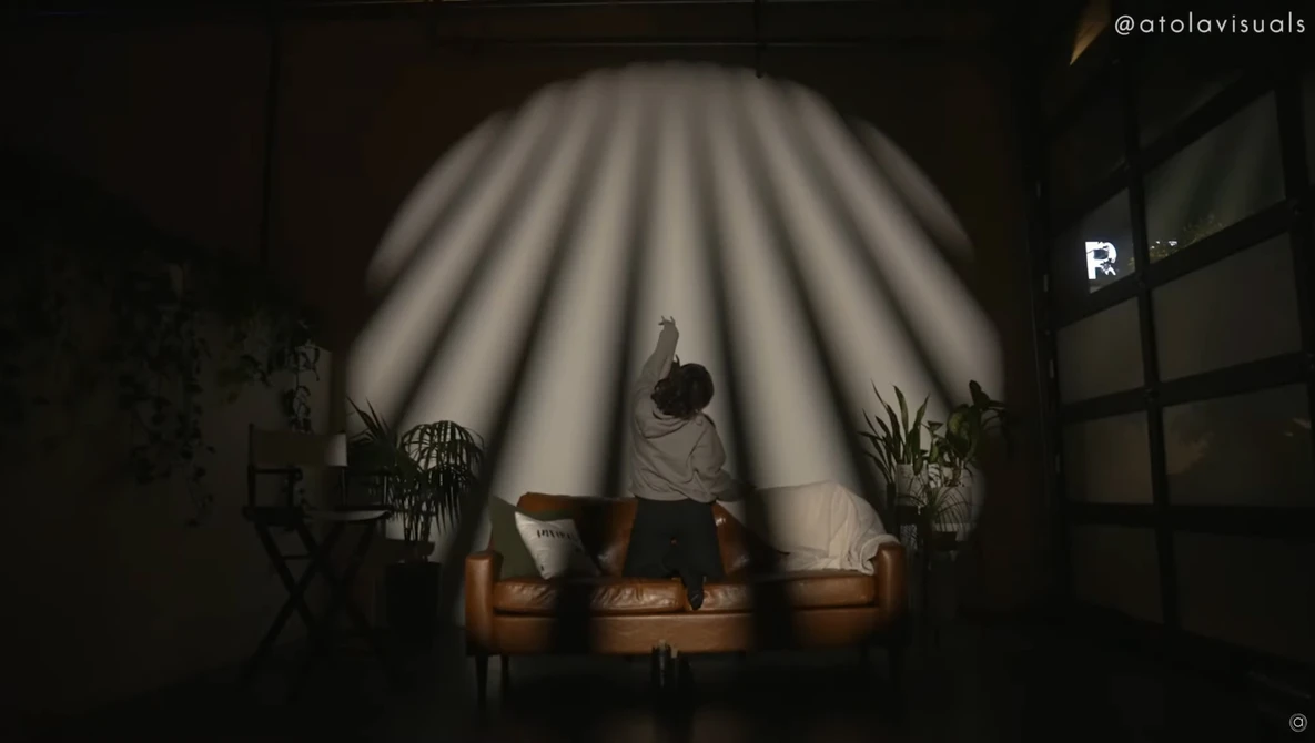Person sitting on a brown leather couch under dramatic radial light rays in a dark interior space.