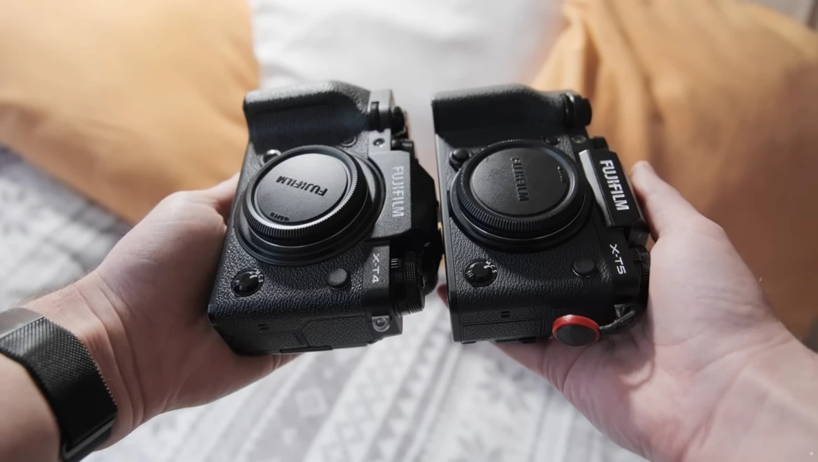 Two compact mirrorless cameras held side by side in hands, showing their top plates and lens mounts.