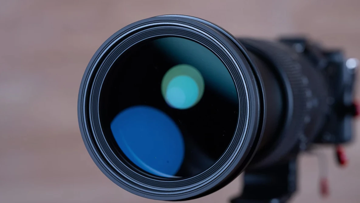 Close-up of a camera lens front element showing internal blue and cyan reflections against a dark background.