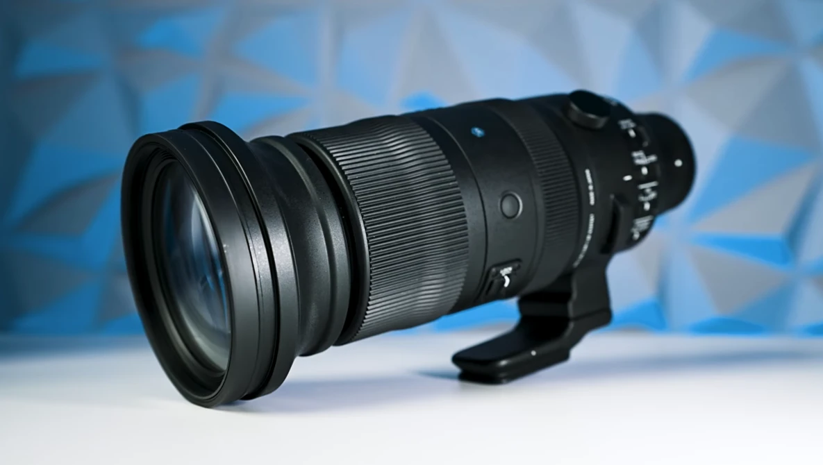 Black telephoto lens with extended barrel and control rings mounted on white surface against blue background.