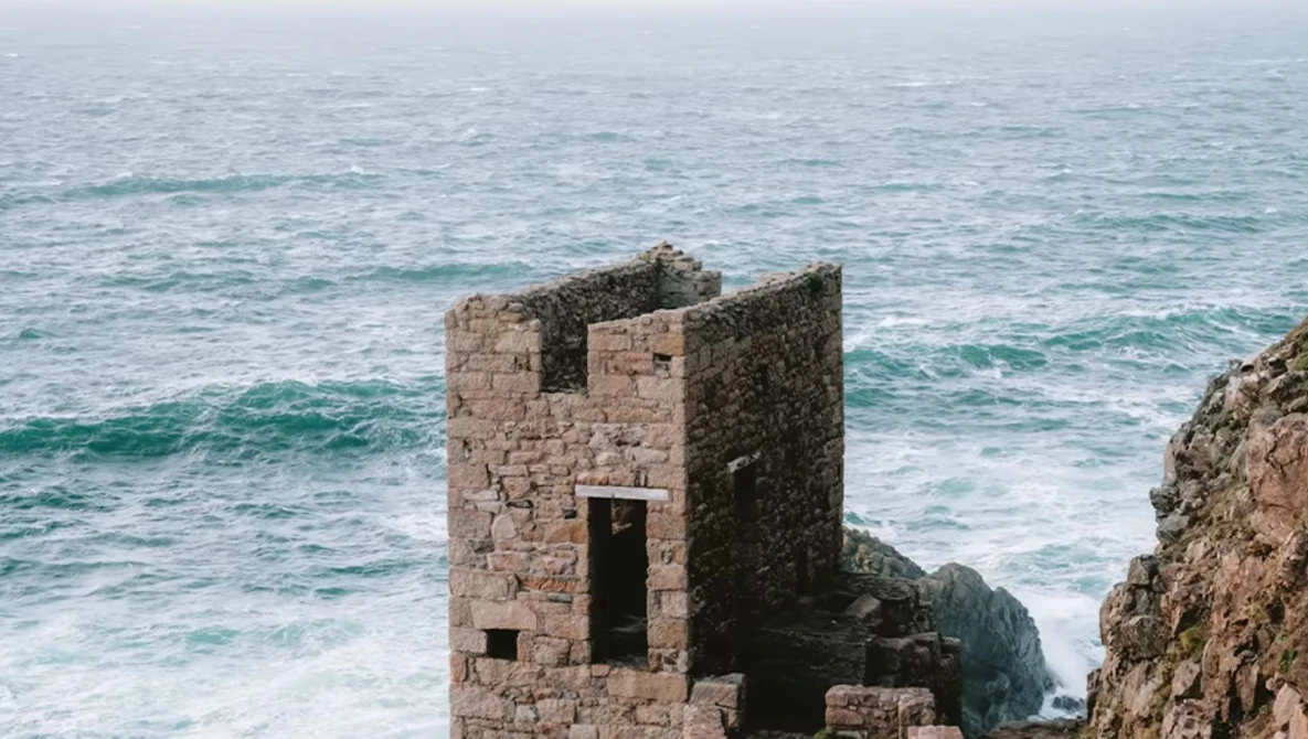 Weathered stone tower ruins on a rocky coastal cliff overlooking turbulent ocean waves.