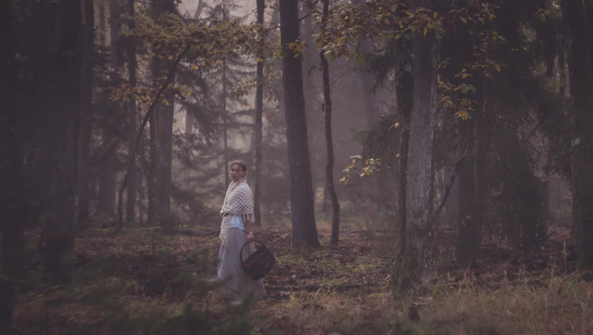 Woman in white shirt standing among tall trees in misty forest during autumn.