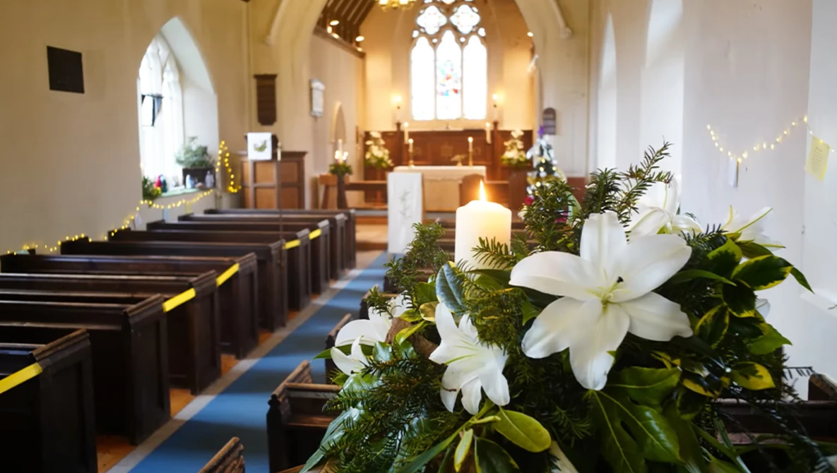 White lilies with greenery arranged in the foreground of a church aisle decorated for a wedding ceremony.