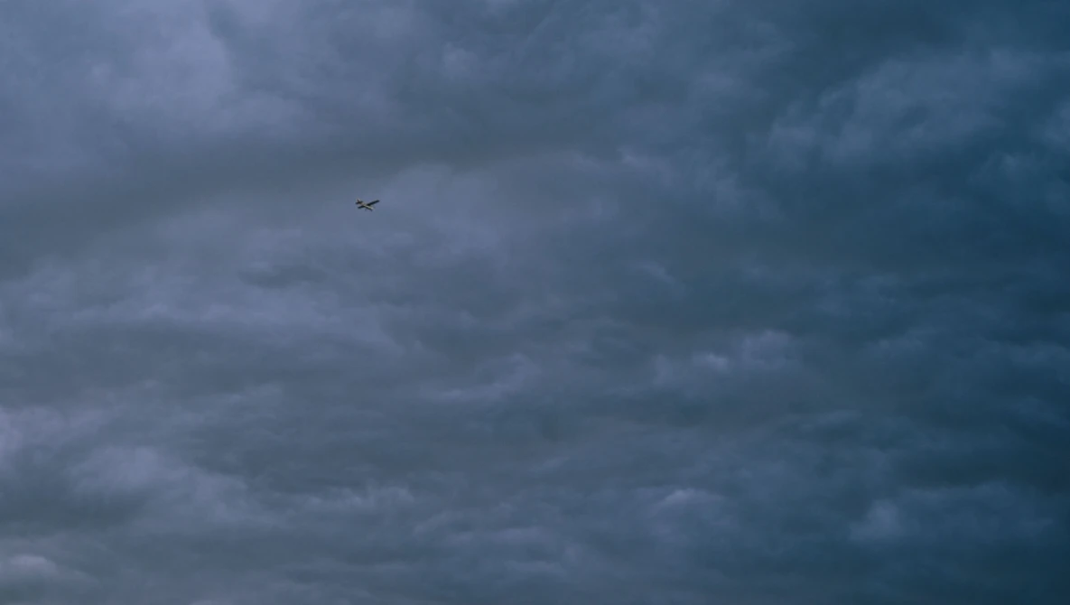 Small aircraft silhouette flying through dramatic storm clouds at dusk.