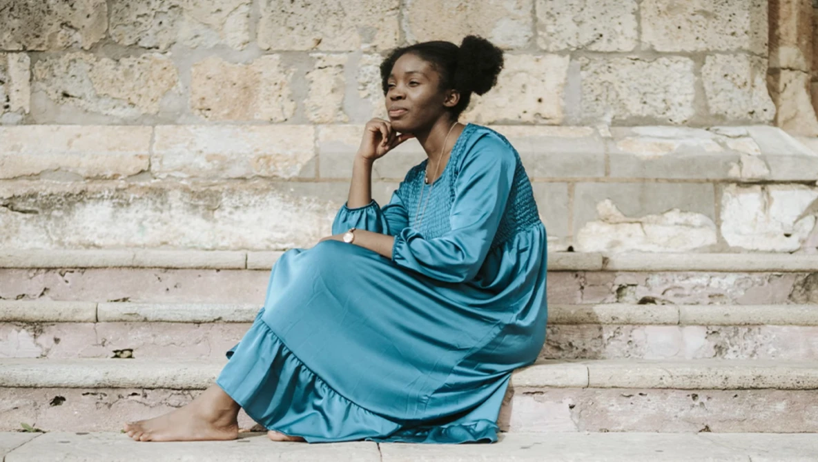Woman in blue dress sitting on stone steps against weathered brick wall.