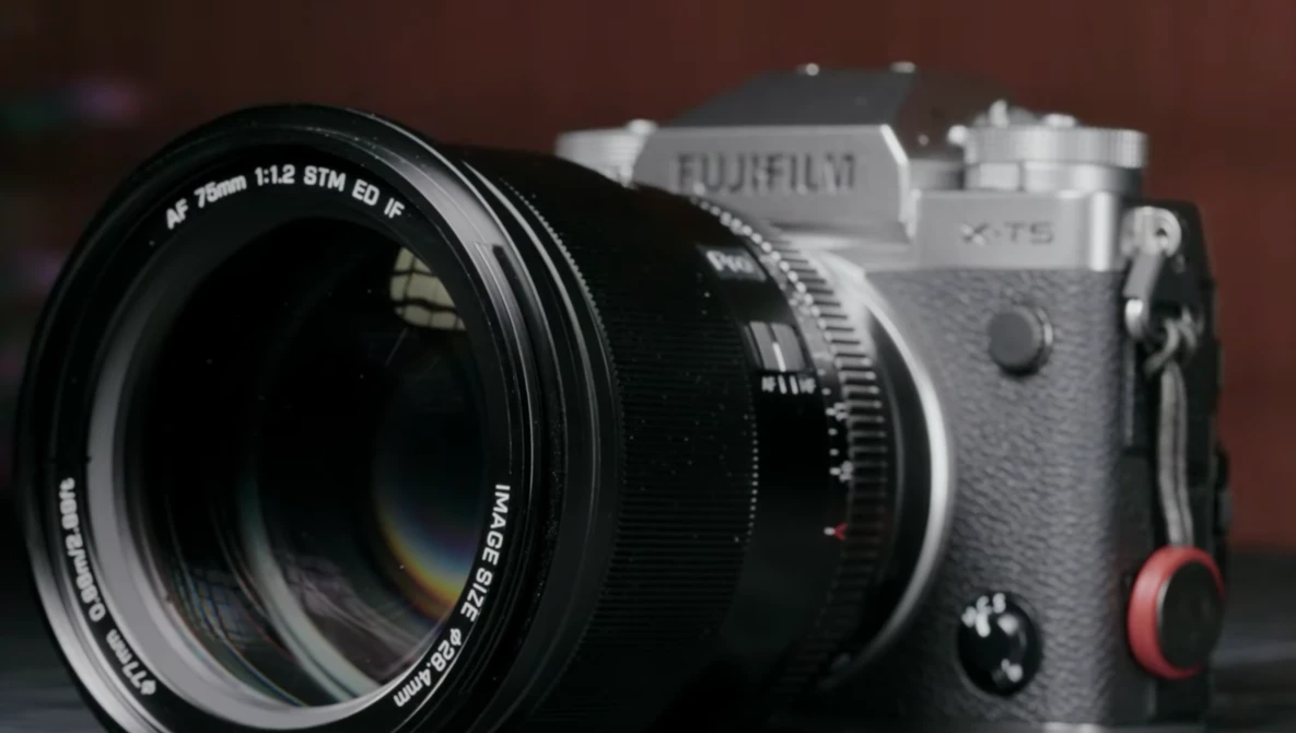 Fujifilm X-T5 camera with 75mm prime lens attached, shown in three-quarter view against a dark red background.