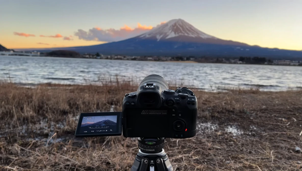 Camera on tripod with articulating monitor displays snowy landscape and mountain at twilight.