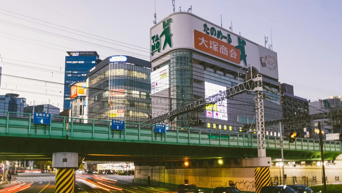 Urban intersection at dusk with elevated highway overpass and illuminated commercial buildings with Japanese signage.