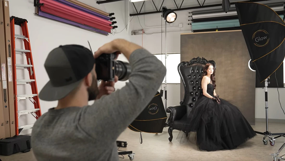 Photographer shooting a portrait subject seated in an ornate black chair in a professional studio setup.