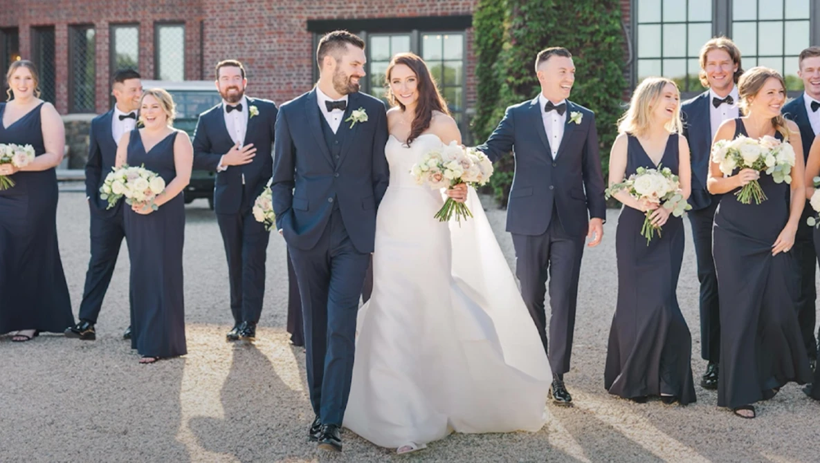 Wedding party lined up outdoors with bride and groom in center, bridesmaids and groomsmen flanking them in formal attire.