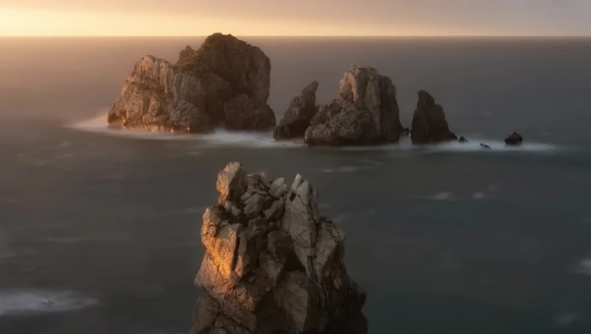 Rocky sea stacks silhouetted against golden sunrise light over misty ocean waters.
