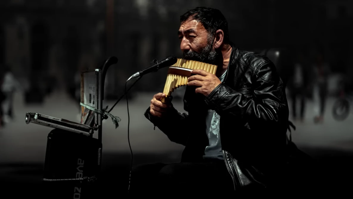 Musician performing with pan flute at microphone in dark venue with blurred background.