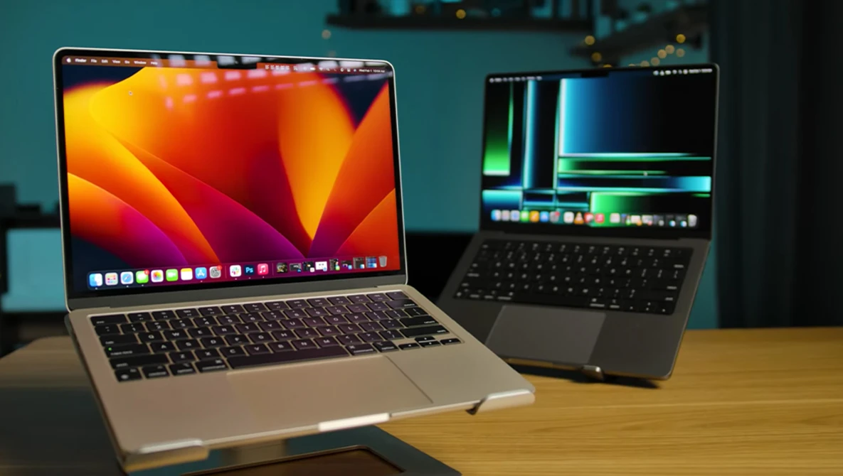Two laptops on a wooden table displaying video editing software with colorful waveforms and timelines.