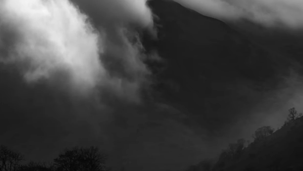 Dramatic black and white landscape with roiling storm clouds and silhouetted terrain below.