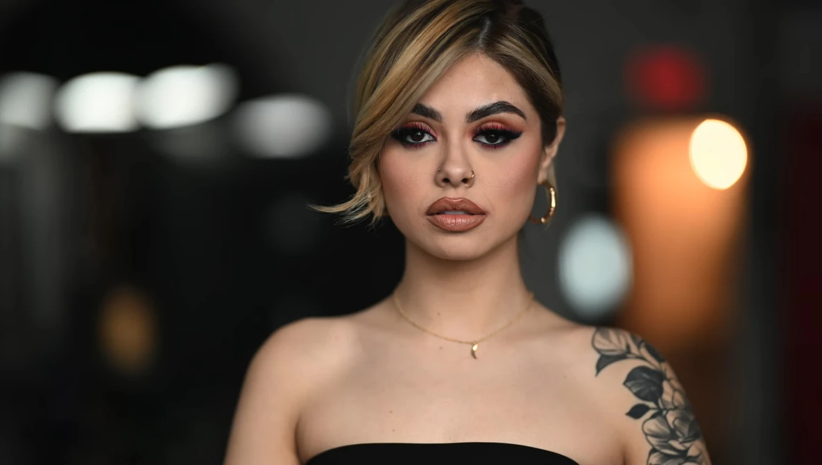 Portrait of a woman with short blonde hair and shoulder tattoo against blurred nighttime background.