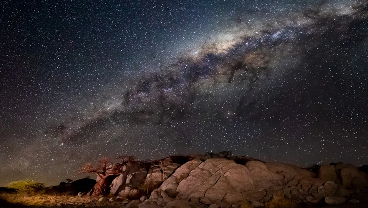 Milky Way galaxy stretching across night sky above desert rock formations.