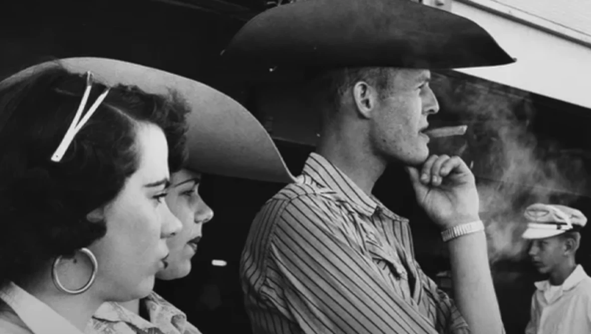 Black and white photograph of people in a vehicle, with a man in a cowboy hat smoking a cigar in profile.