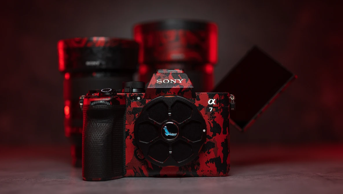 Sony Alpha camera with red and black textured body and matching accessories arranged on dark red background.