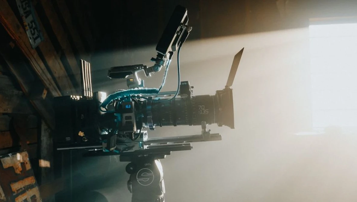 Professional cinema camera with mounted lens and shoulder rig setup lit by bright window light.