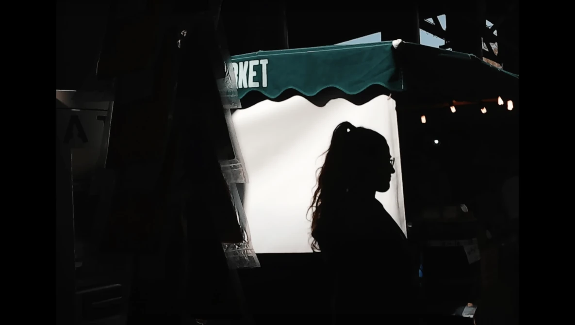 Silhouetted person viewed through a brightly lit storefront window with teal awning at night.