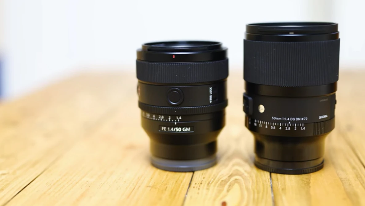 Two camera lenses positioned side by side on a wooden surface, showing their front elements and focus rings.