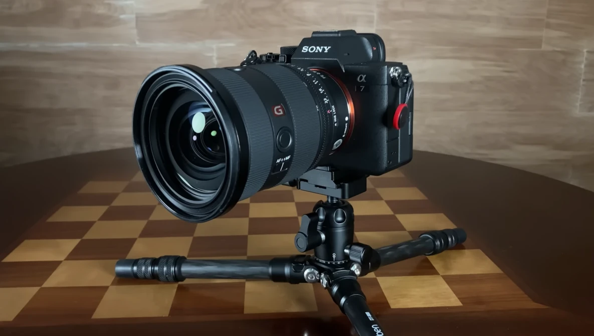 Sony mirrorless camera with wide-angle lens mounted on tripod with ball head against checkered backdrop.