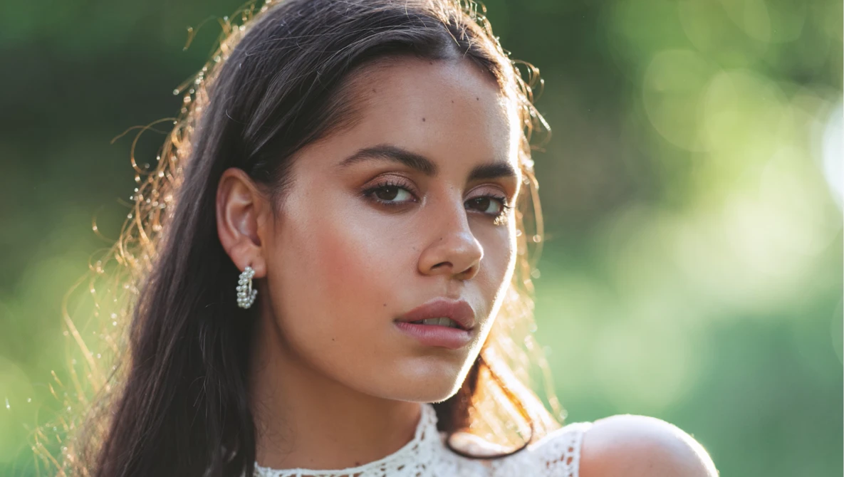 Young woman with long dark hair gazing downward in golden hour sunlight.