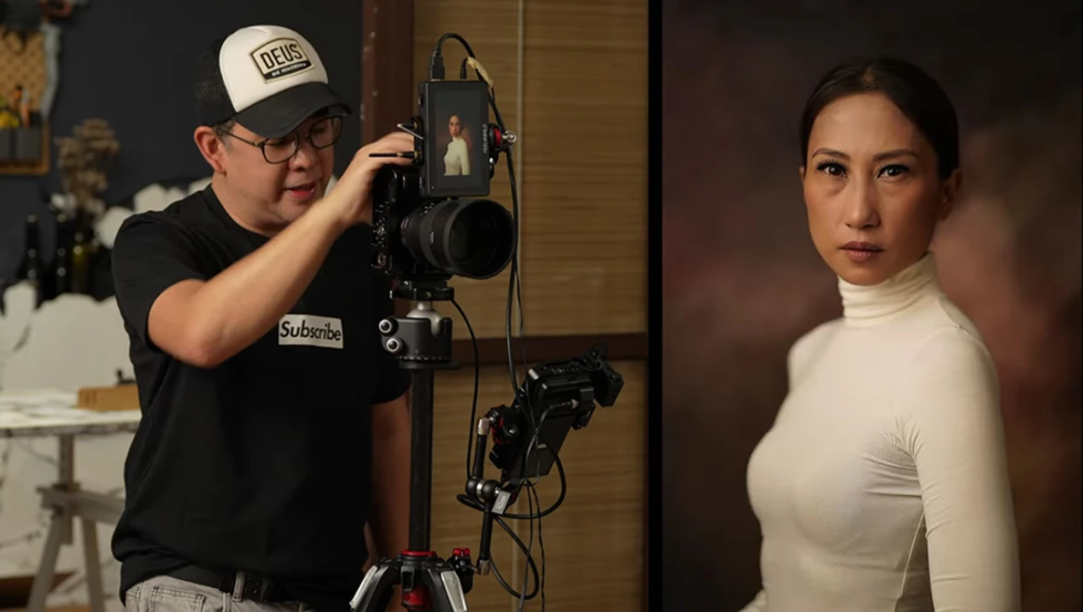 Photographer adjusting a studio light setup while shooting a portrait of a woman in a white turtleneck.