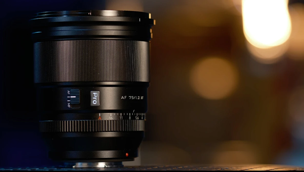Black telephoto lens with autofocus markings, shot against warm bokeh background lighting.