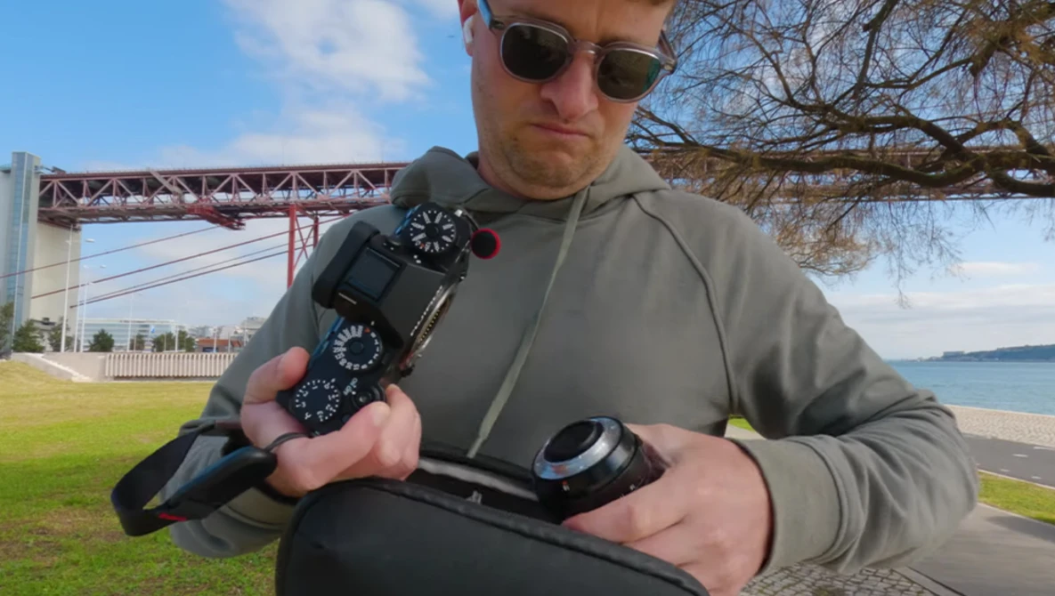 Photographer holding camera gear and wireless transmitter outdoors near a bridge and waterfront.